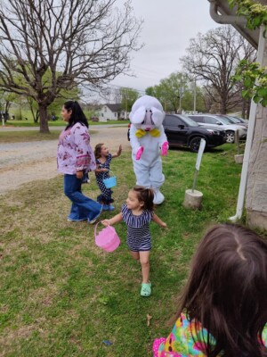 Three girls and Easter bunny participating in Easter egg hunt in church yard
