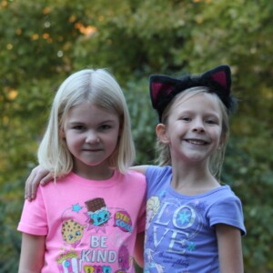 Two kids standing side by side with arm hanging on the others shoulder